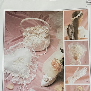 May include: A McCall's sewing pattern for a bridal ensemble, featuring a white satin bag, a lace pillow, a garter, gloves, and a floral headpiece. The pattern number is 2058.