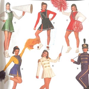 May include: Simplicity Costumes pattern showing cheerleading and marching band outfits. The costumes include dresses, skirts, and jackets in green, red, white, yellow, and blue. The pattern includes sizes 14, 16, and 18.