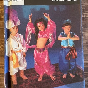 May include: Simplicity pattern for children's costumes. The pattern includes three costumes: a genie, a belly dancer, and a prince. The costumes are shown on three children. The pattern is labeled "Simplicity Costumes" and "Pattern/Patron".