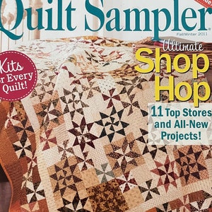 Könnte beinhalten: Ein Magazincover mit einem Quiltmuster mit verschiedenen Mustern in Braun, Rot und Weiß. Das Magazin heißt "Quilt Sampler" und der Untertitel lautet "Ultimate Shop Hop". Das Cover enthält auch den Text "Kits for Every Quilt!" und "11 Top Stores and All-New Projects!"