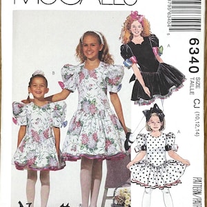 Puede incluir: Patrón de costura McCall's con tres diseños de vestidos para niñas. Los vestidos presentan estampados florales, lunares y negro liso. El patrón incluye la marca "Nannette" e información sobre tallas.