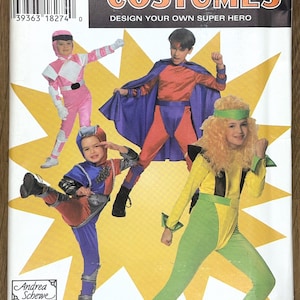 May include: Simplicity Costumes pattern featuring children in superhero costumes. The cover displays a pink Power Ranger, a superhero with a red and blue outfit, and a yellow and green superhero. The text reads "DESIGN YOUR OWN SUPER HERO".
