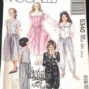 May include: A McCall's sewing pattern envelope with illustrations of children's clothing. Designs include dresses and a jumpsuit. The text "Fashion Basics for Kids" is displayed. Measurements are in inches.