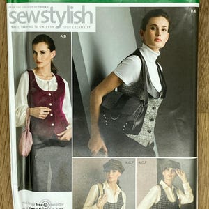 Peut inclure: Une pochette de patron de couture Simplicity 2862 pour gilets en tailles H5 6, 8, 10, 12, 14. L'emballage présente des illustrations de gilets dans divers tissus, notamment un gilet en velours bordeaux, un gilet à chevrons et des gilets à carreaux.