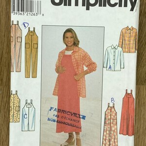 Op de afbeelding: Simplicity naaipatroon 8011 voor zwangerschapskleding. Het patroon bevat opties voor overalls, jurken en shirts. De voorkant van de verpakking toont een vrouw die een jurk en een geruit shirt draagt. De tekst "Simplicity" en "Fabricville".