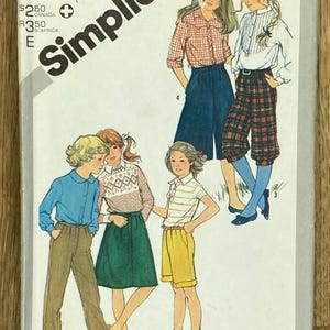 Puede incluir: Sobre de patrón de costura Simplicity vintage con ilustraciones de ropa infantil. La portada muestra dibujos de niñas con varios conjuntos, incluyendo pantalones cortos, faldas y pantalones. El sobre incluye texto que indica la talla y el nombre de la marca.