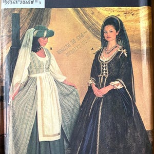 Puede incluir: Un sobre de patrón de costura Simplicity Costumes 7756 con dos vestidos de estilo histórico. La vista A es un vestido oscuro estampado con velo y tocado. La vista B es un vestido a rayas con delantal liso, mangas largas y un sombrero a juego.