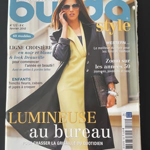 Op de afbeelding: Een tijdschriftcover met een vrouw met een zonnebril en een zwarte jas over een gele jurk. De titel van het tijdschrift is "buda style" met Franse tekst. De cover bevat de tekst "LUMINEUSE au bureau" en de datum "février 2010".