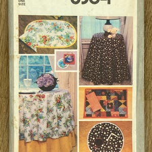 Może przedstawiać: Vintage wzór Simplicity 8364 przedstawiający różne projekty dekoracji wnętrz. Wzór zawiera instrukcje dotyczące obrusu, podkładek i innych przedmiotów z kwiatowymi i groszkowymi wzorami. Wzór jest oznaczony "ONE SIZE".