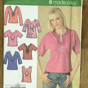 May include: A Simplicity 4124 sewing pattern envelope for tops in sizes U5 16, 18, 20, 22, 24. The cover features illustrations of six different top variations with V-necklines and a photograph of a pink top with a decorative trim.