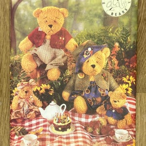 Puede incluir: Un sobre de patrón Butterick vintage con osos de peluche con varios atuendos, incluyendo una chaqueta roja y un vestido azul. Los osos están colocados sobre una manta de picnic con un pastel, un juego de té y fresas. El texto "5029 Butterick" está en la parte superior.