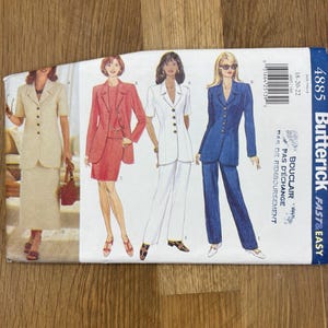 May include: A Butterick sewing pattern envelope featuring illustrations of women's suits in various colors: beige, red, white, and blue. The pattern number is 4885, with text indicating sizes 18-20-22. The envelope is on a wooden surface.