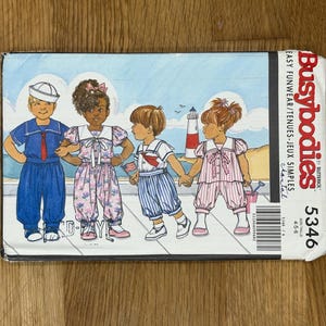 Peut inclure: Un patron de couture vintage intitulé "Busybodies 5346" avec des illustrations d'enfants en tenues de marin et de plage. La couverture représente quatre enfants sur une plage avec un phare en arrière-plan. Le patron est pour les tailles 4-5-6.