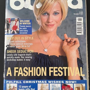 Op de afbeelding: Een modebladcover met een blonde vrouw met blauwe ogen. De cover bevat de tekst "WORLD OF FASHION" en "A FASHION FESTIVAL". Extra tekst omvat "WELCOME IN WINTER!" en "FULFILL CHRISTMAS WISHES NOW!"