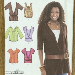 Op de afbeelding: Simplicity naaipatroon 3790 voor tops in maten R5 14, 16, 18, 20, 22. De verpakking bevat illustraties van zes verschillende topontwerpen met variërende halslijnen, mouwlengtes en patronen, naast een foto van een bruine top met overslag.