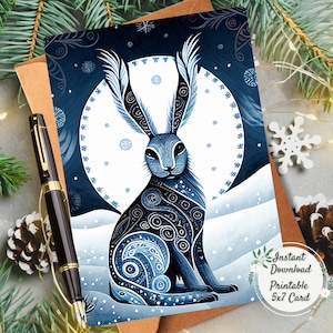 Könnte beinhalten: Eine blau-weiße Wintergrußkarte mit einem stilisierten Hasen mit kunstvollen Mustern. Die Karte ist ein druckbarer Sofort-Download im Format 12,7 x 17,8 cm. Ein Stift, Tannennadeln und eine Schneeflocke befinden sich im Hintergrund.