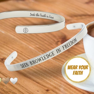 May include: Two silver bracelets with engraved messages. The top bracelet reads "Seek the Truth in Love". The bottom bracelet reads "Seek Knowledge in Freedom". A gold circle with the text "Wear Your Faith" is in the foreground.