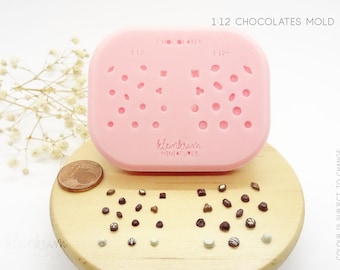 Puede incluir: Un molde de silicona rosa para hacer chocolates en miniatura. El molde tiene una variedad de formas, incluyendo círculos, cuadrados y diamantes. El molde está etiquetado como "1:12 Chocolates Mold" y "Klenkram Miniatures".