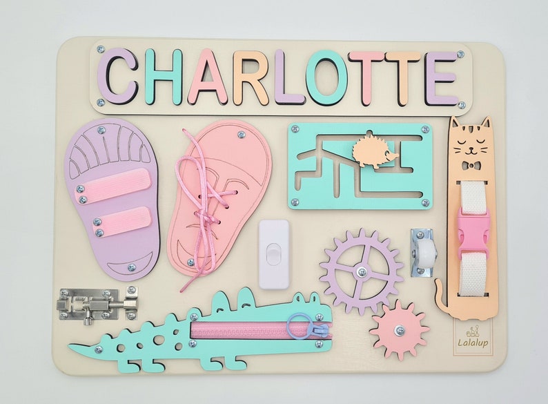 May include: A wooden activity board with a variety of textures and activities for children. The board features a nameplate with the name "CHARLOTTE" in colorful letters, a zipper, a latch, a toggle switch, a gear, a wheel, a shoe with laces, a shoe with straps, a maze, and a buckle. The board is made of natural wood and is painted in pastel colors.