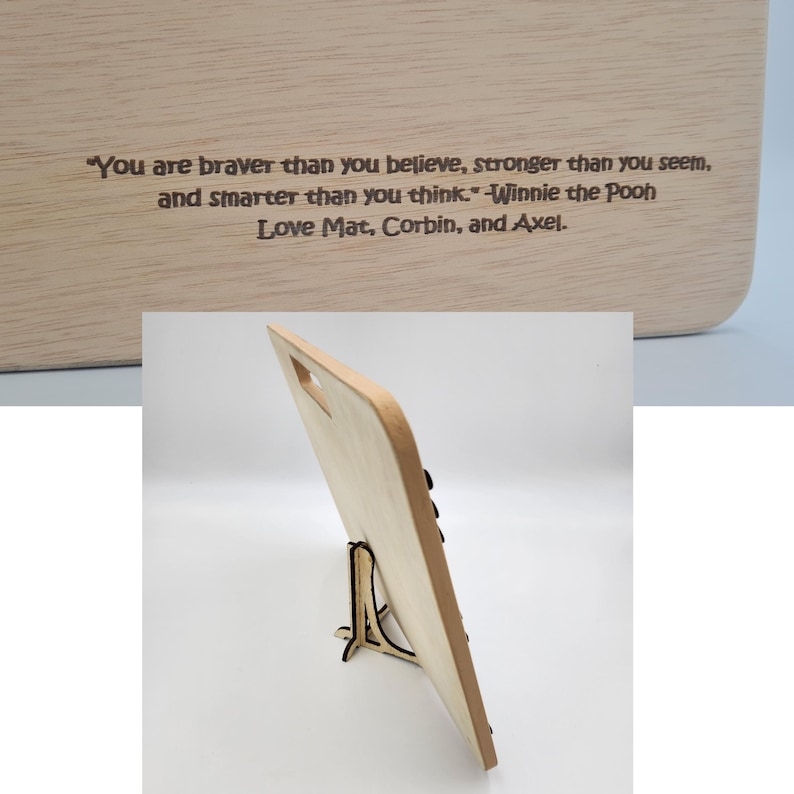 May include: A wooden cutting board with a stand, featuring an engraved quote from Winnie the Pooh: "You are braver than you believe, stronger than you seem, and smarter than you think." The board is signed "Love Mat, Corbin, and Axel."
