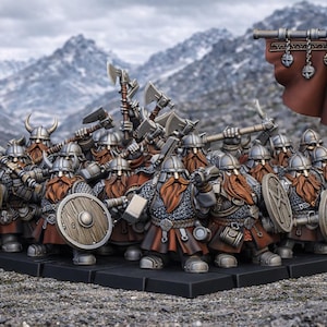 Könnte beinhalten: Eine Gruppe von Miniatur-Zwergenkriegern, bewaffnet mit Äxten, Schilden und Helmen. Sie haben rote Bärte und posieren vor einer bergigen Kulisse. Ein Banner mit einem Symbol wird hochgehalten.