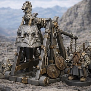 Może przedstawiać: Szczegółowy miniaturowy model broni oblężniczej, trebuszetu, ze skomplikowanymi rzeźbami i detalami lin. W pobliżu stoją dwie miniaturowe figurki brodatych wojowników. Model osadzony jest na tle górzystego krajobrazu.