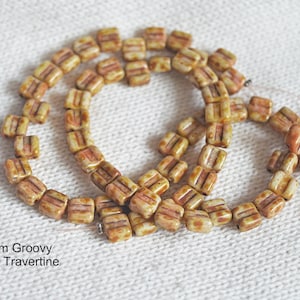 May include: A strand of 6mm square ceramic beads in a light brown color with darker brown streaks. The beads are arranged in a circular pattern, with some beads overlapping. The text "6mm Groovy Dark Travertine" is visible at the bottom of the image.
