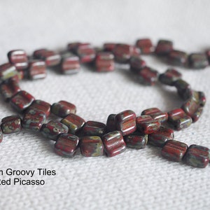 May include: A strand of 6mm red, green, and brown glass tiles. The tiles are square with rounded edges and have a speckled pattern. The text "6mm Groovy Tiles Red Picasso" is visible in the image.