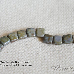 May include: A close-up of a string of frosted green glass tiles. The tiles are square and have a mottled, cloudy appearance. The text "Czechmate 6mm Tiles Frosted Chalk Lumi Green" is visible below the tiles.
