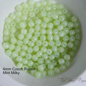 May include: A bowl of 4mm round Czech glass beads in a light green, milky color. The beads are opaque and have a slightly frosted finish.
