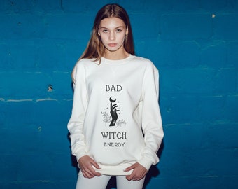 May include: White sweatshirt with a black graphic design that says "Bad Witch Energy" and features a hand holding a crescent moon.