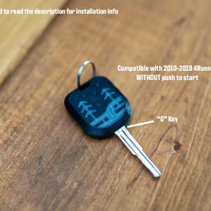 May include: A black car key with a metal blade and a plastic head featuring a light blue graphic of trees and a landscape. Text on the image reads: It is recommended to read the description for installation info, Compatible with 2010-2019 4Runner WITHOUT push to start, and G Key.