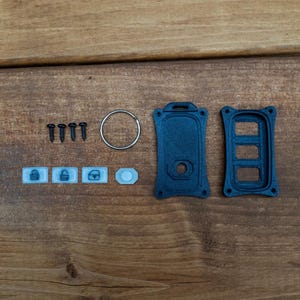 May include: A black plastic key fob replacement shell with two main housing pieces, four small black screws, a silver metal keyring, and four small white rubber button inserts featuring icons for locking, unlocking, and a trunk release.