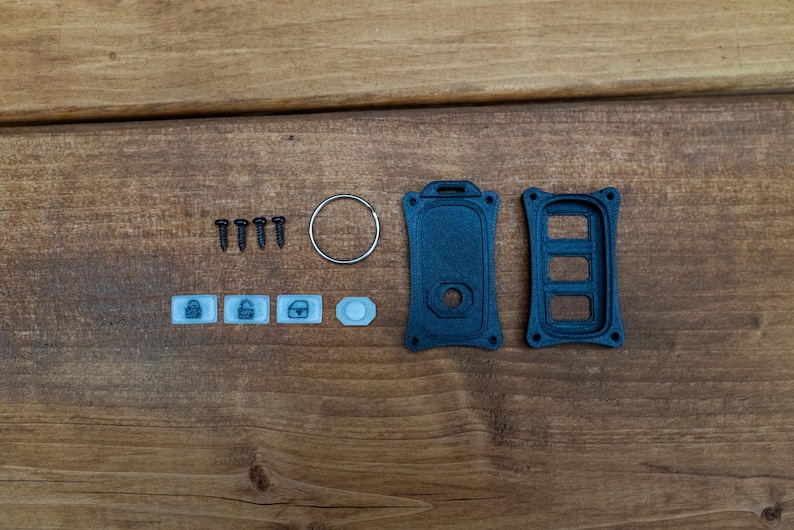 May include: A black plastic key fob replacement shell with two main housing pieces, four small black screws, a silver metal keyring, and four small white rubber button inserts featuring icons for locking, unlocking, and a trunk release.