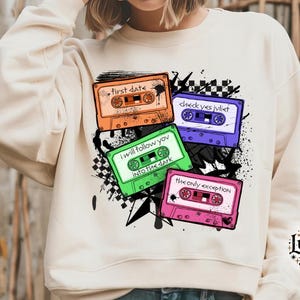 Puede incluir: Una sudadera blanca con un diseño gráfico de cuatro cintas de cassette con diferentes fondos y textos de colores. El texto en las cintas dice "first date", "i will follow you into the dark", "check yes jvliet", y "the only exception".