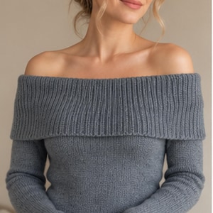 May include: A slate blue long-sleeve sweater featuring an off-the-shoulder neckline with a wide, ribbed knit fold-over collar. The garment is constructed from a textured knit fabric that extends down the sleeves and across the chest area.
