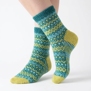May include: A pair of knitted socks with a geometric pattern. The socks feature a teal cuff, heel, and toe, with a yellow and light blue pattern on the body. The socks are displayed on a person's legs against a white background.