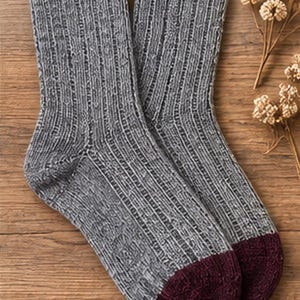 Peut inclure: Une paire de chaussettes mi-mollet présentant un motif en tricot côtelé gris texturé sur toute la longueur de la jambe et du pied. Les chaussettes sont terminées par une pointe de couleur bordeaux foncé unie, contrastant avec le tissu gris chiné.