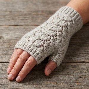May include: A light gray knitted fingerless glove with a detailed leaf pattern. The glove is made of soft yarn and has a ribbed cuff. The design allows for full finger movement while keeping the hand warm.