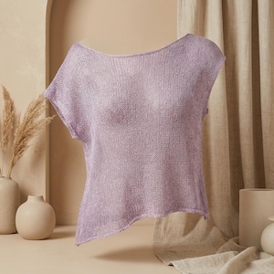 Pode incluir: Uma blusa de manga curta e corte largo na cor lavanda claro. A peça apresenta um decote largo e aberto com uma textura de malha aberta semitransparente. A bainha é assimétrica, com um lado mais comprido que o outro, criando uma silhueta relaxada.
