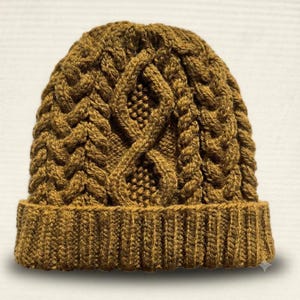 Pode incluir: Um gorro de malha cor de mostarda com um padrão de tranças proeminente, texturas verticais entrelaçadas e um motivo central de diamante. O gorro inclui uma bainha canelada espessa na base, feita de um material de fio denso e texturizado.