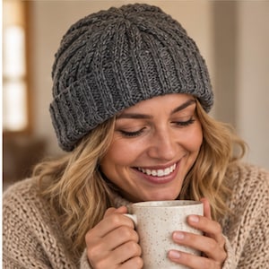 May include: A dark gray knit beanie featuring a ribbed texture and a folded cuff. The hat is constructed with a thick, warm yarn material and displays a consistent vertical pattern throughout the crown, providing a snug fit around the head.