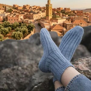 May include: A pair of light blue, ribbed knit socks worn on the feet. The socks feature a vertical textured pattern that runs from the cuff down to the toe area, providing a consistent knit appearance throughout the garment.