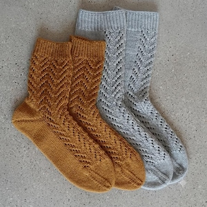 May include: Two pairs of knitted socks, one pair in mustard yellow and one pair in light gray. Each sock features a ribbed cuff and a vertical chevron lace pattern that extends from the cuff down to the toe, with a solid knit heel and toe.