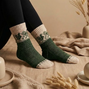 May include: A pair of mid-calf knit socks featuring a solid dark green foot and toe section in a light beige hue. The upper cuff and ankle area display a decorative band with a repeating dark green bird motif on a light beige background.