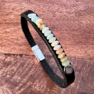 May include: A black leather bracelet with a silver clasp and a row of colorful gemstone beads.