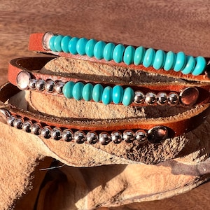 May include: Three leather bracelets with turquoise beads and silver accents. The bracelets are stacked on top of each other.