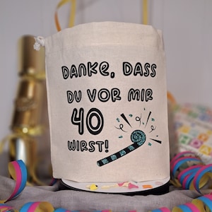 May include: A white fabric bag with a drawstring closure. The bag has a black graphic that says "Danke. Dass du vor mir 40 wirst!" with a blue and black party blower graphic.