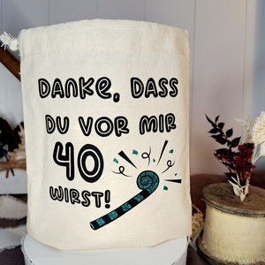 May include: A white canvas bag with a black and white design that says "Danke, dass du vor mir 40 wirst!" with a green and black party blower graphic.
