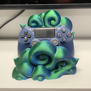 May include: A 3D printed controller stand in the shape of a green and blue cloud. The stand is designed to hold a Playstation 4 controller.